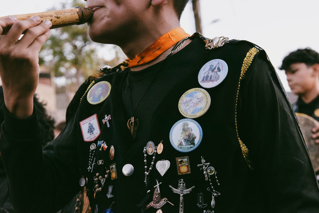 A musician in Chile playing a traditional whistle, adorned in a vest with cultural pins.